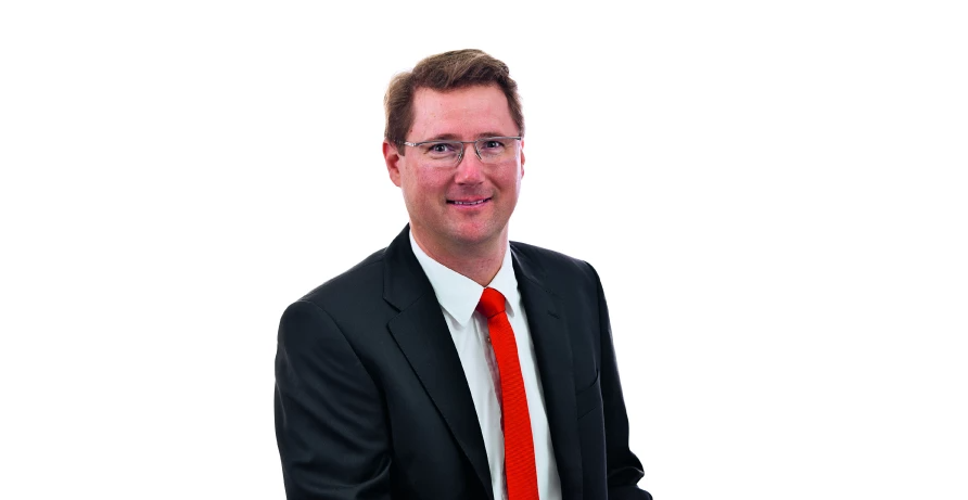 Porträt eines Geschäftsmanns im Anzug mit weißem Hemd, schwarzem Sakko und roter Krawatte vor weißem Hintergrund.