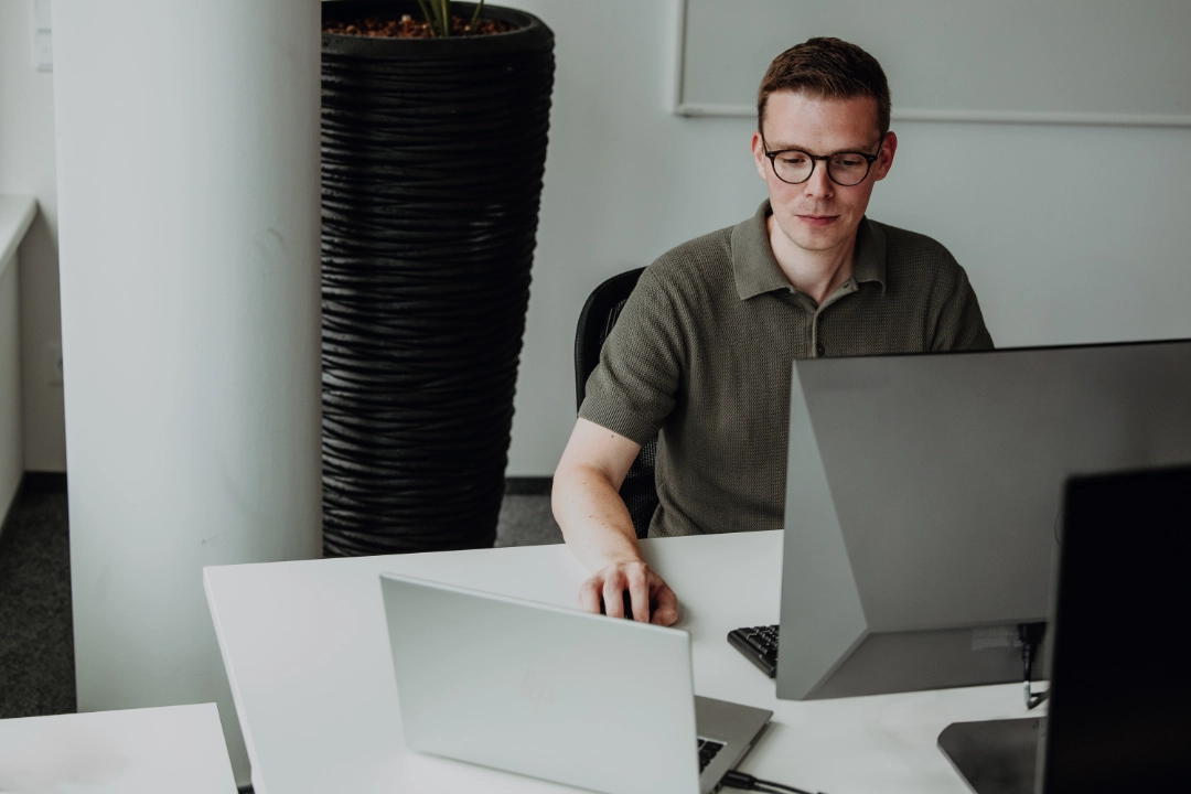 Mitarbeitender arbeitet fokussiert am Laptop und Monitor im modernen Büro – eigenverantwortliches Arbeiten, fachliche Expertise und attraktive Entwicklungsperspektiven für Berufserfahrene bei BSI Software.