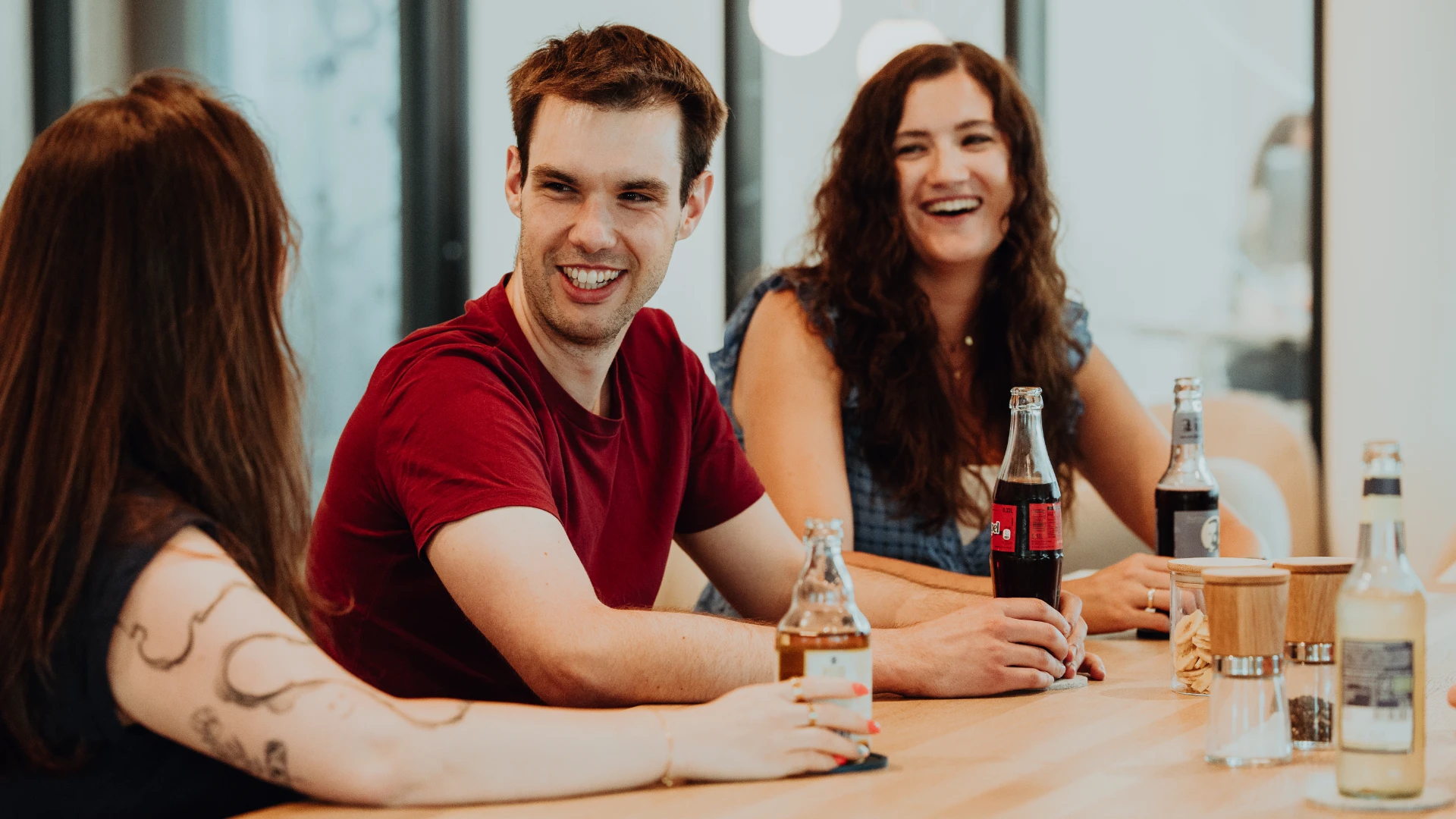 Drei Mitarbeitende sitzen entspannt zusammen, lachen und tauschen sich bei Getränken aus – eine offene, kollegiale Atmosphäre und gelebte Teamkultur bei BSI Software, die den Arbeitsalltag attraktiv und menschlich macht.