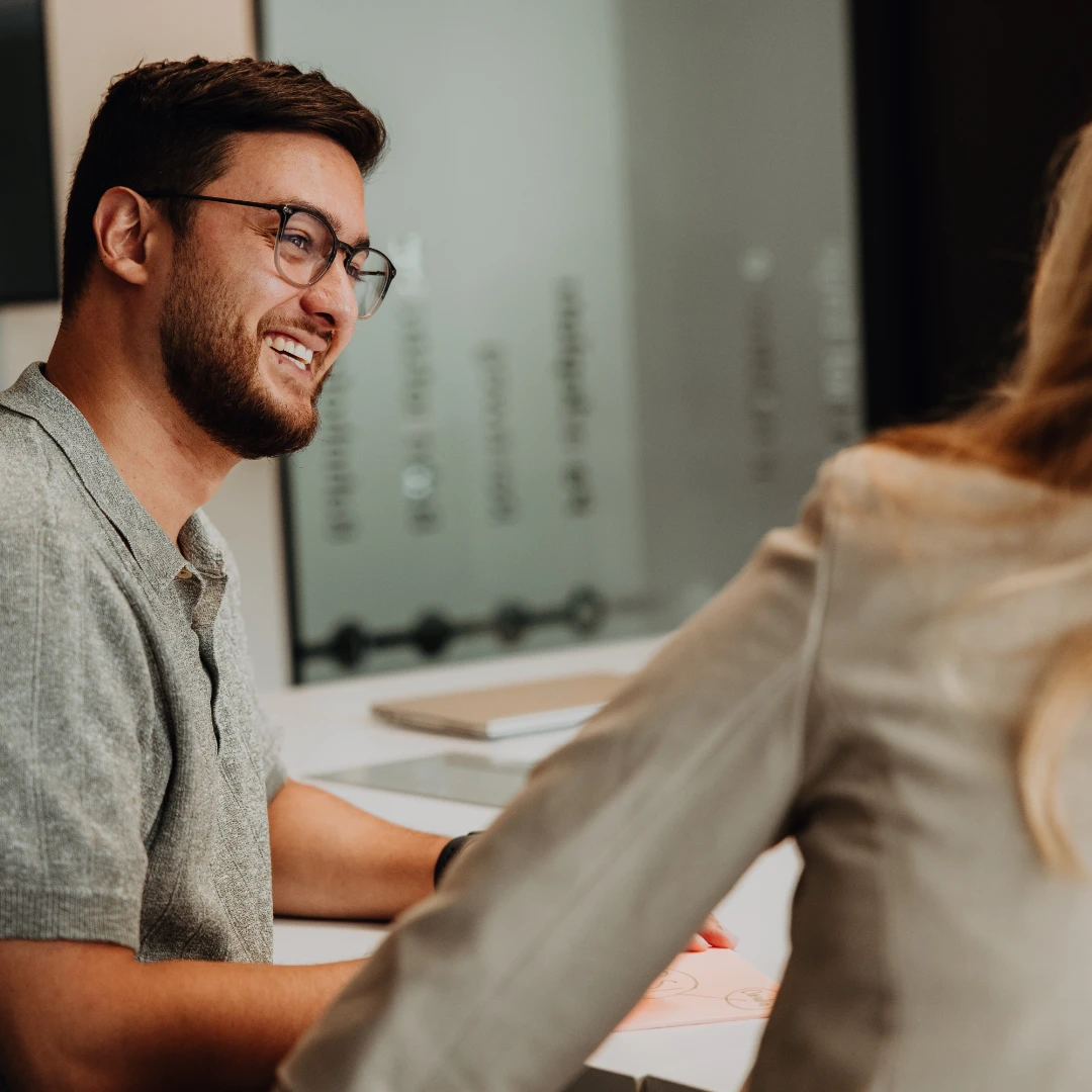 Zwei Mitarbeitende im Gespräch am Tisch, lachen und tauschen sich aus – offener Austausch, persönliche Entwicklung und ein unterstützendes Umfeld für den erfolgreichen Berufseinstieg bei BSI Software.