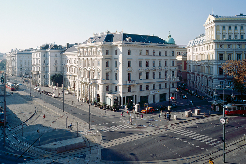 Historische Straßenszene in Wien mit prächtigen Gründerzeit-Gebäuden, Straßenbahnen und breiten Kreuzungen bei klarem Himmel.