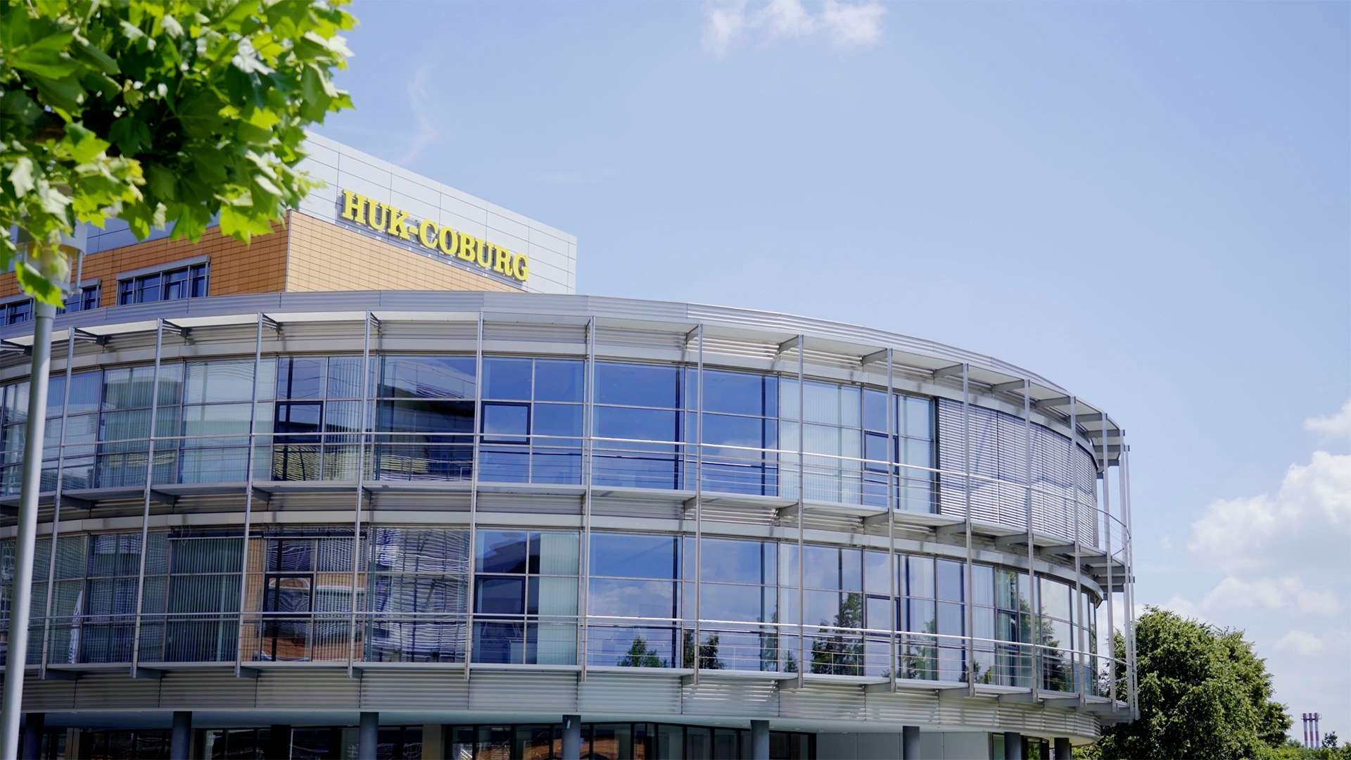 Moderne Glasfassade des HUK-COBURG Unternehmenssitzes mit gut sichtbarem Logo auf dem Dach.