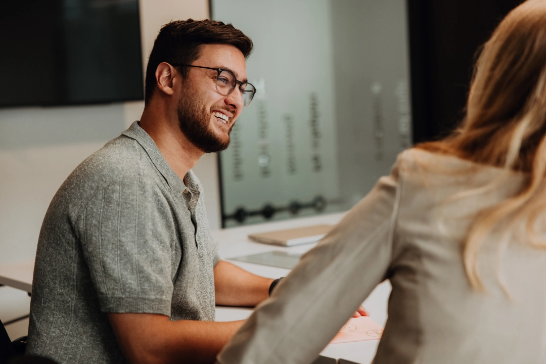 Zwei Mitarbeitende im Gespräch am Tisch, lachen und tauschen sich aus – offener Austausch, persönliche Entwicklung und ein unterstützendes Umfeld für den erfolgreichen Berufseinstieg bei BSI Software.