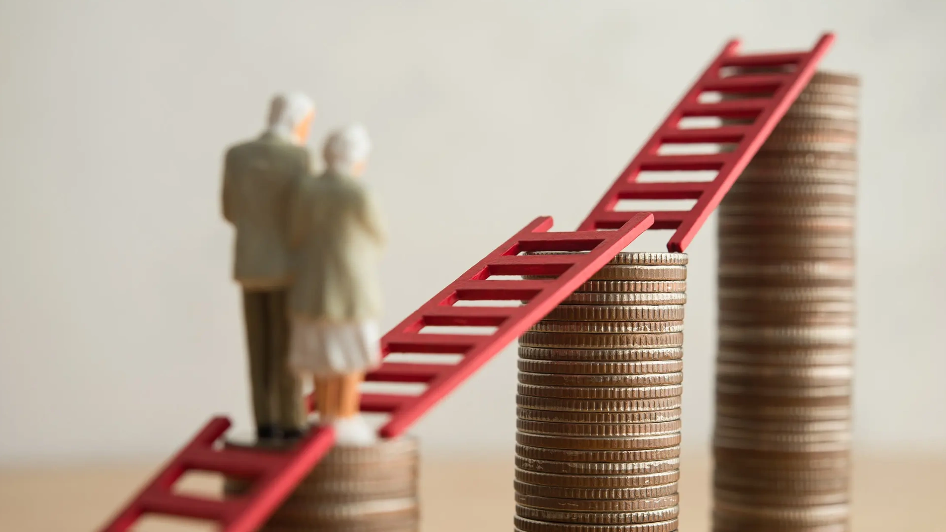 Zwei Miniaturfiguren eines älteren Paares stehen auf einem Münzstapel. Rote Leitern verbinden mehrere unterschiedlich hohe Münzstapel und symbolisieren den langfristigen Vermögensaufbau für die Altersvorsorge. Das Titelbild illustriert ein Interview mit BSI Software Vorstandsmitglied Burkhard Oppenberg über die Chancen des Altersvorsorgedepots für Versicherer.