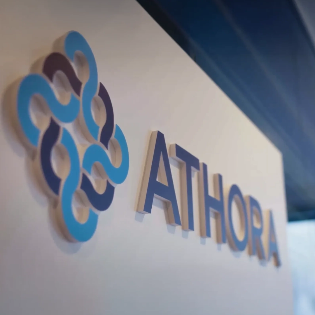 Primo piano del logo Athora blu e turchese su una parete chiara di un ufficio. Athora è cliente di BSI Software e utilizza soluzioni per il Customer Relationship Management digitale e la creazione di esperienze cliente coinvolgenti.