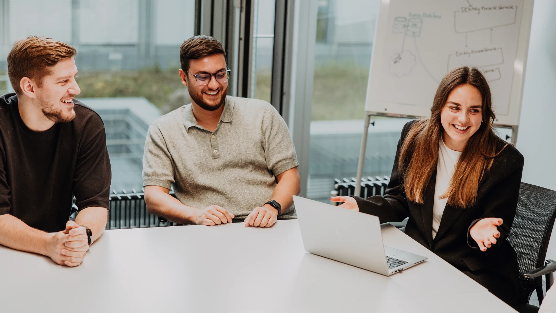 Drei Mitarbeitende sitzen gemeinsam in einem Meetingraum, lachen und diskutieren Ideen am Laptop – eine offene, wertschätzende Teamkultur und moderne Arbeitsumgebung bei BSI Software als attraktiver Arbeitsplatz.