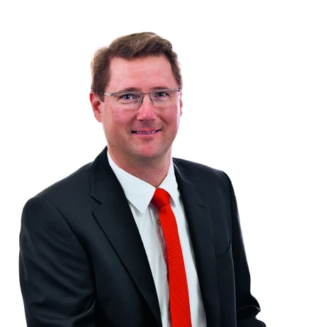 Porträt eines Geschäftsmanns im Anzug mit weißem Hemd, schwarzem Sakko und roter Krawatte vor weißem Hintergrund.