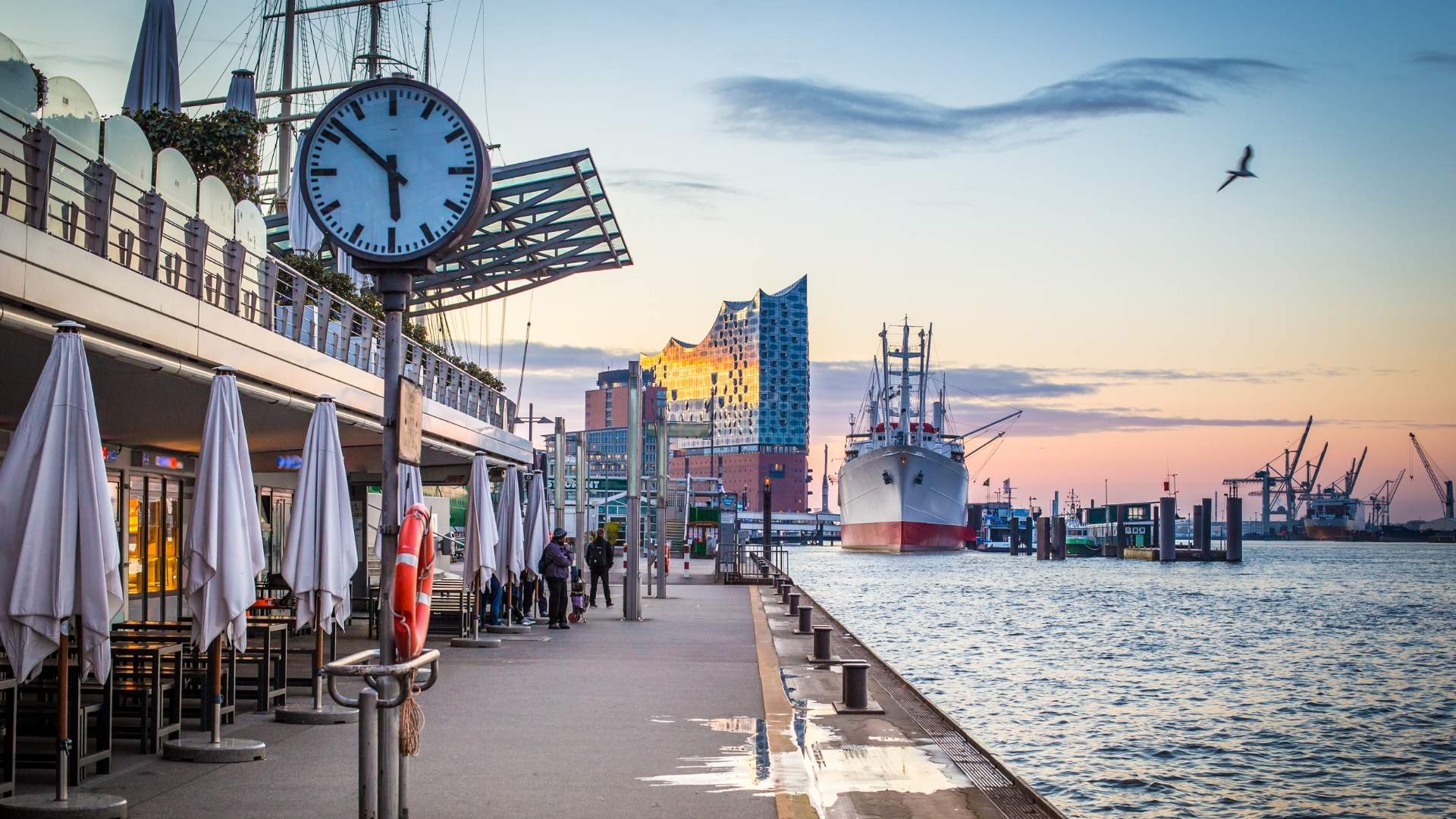 Blick auf die Hamburger Hafenpromenade mit der Elbphilharmonie im Hintergrund, einem historischen Schiff am Anleger und der Elbe im Abendlicht. Hamburg ist der jüngste Standort von BSI Software in Deutschland.