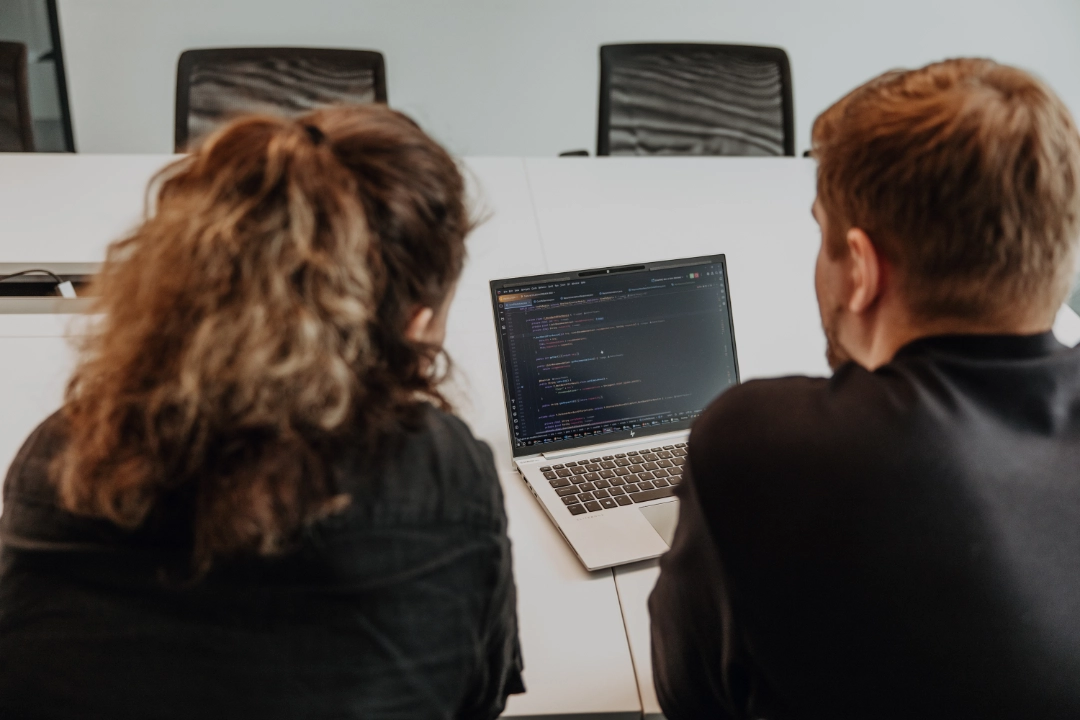 Zwei Mitarbeitende arbeiten gemeinsam am Laptop und analysieren Code – praxisnahe Ausbildung, enge Begleitung und Einblicke in die Softwareentwicklung während der Lehre bei BSI Software in der Schweiz.