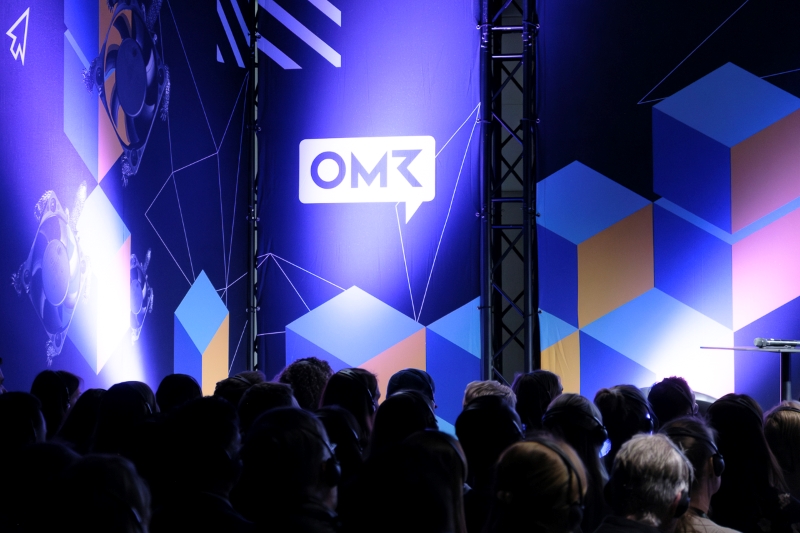 Wand mit dem OMR Logo, davor Menschen