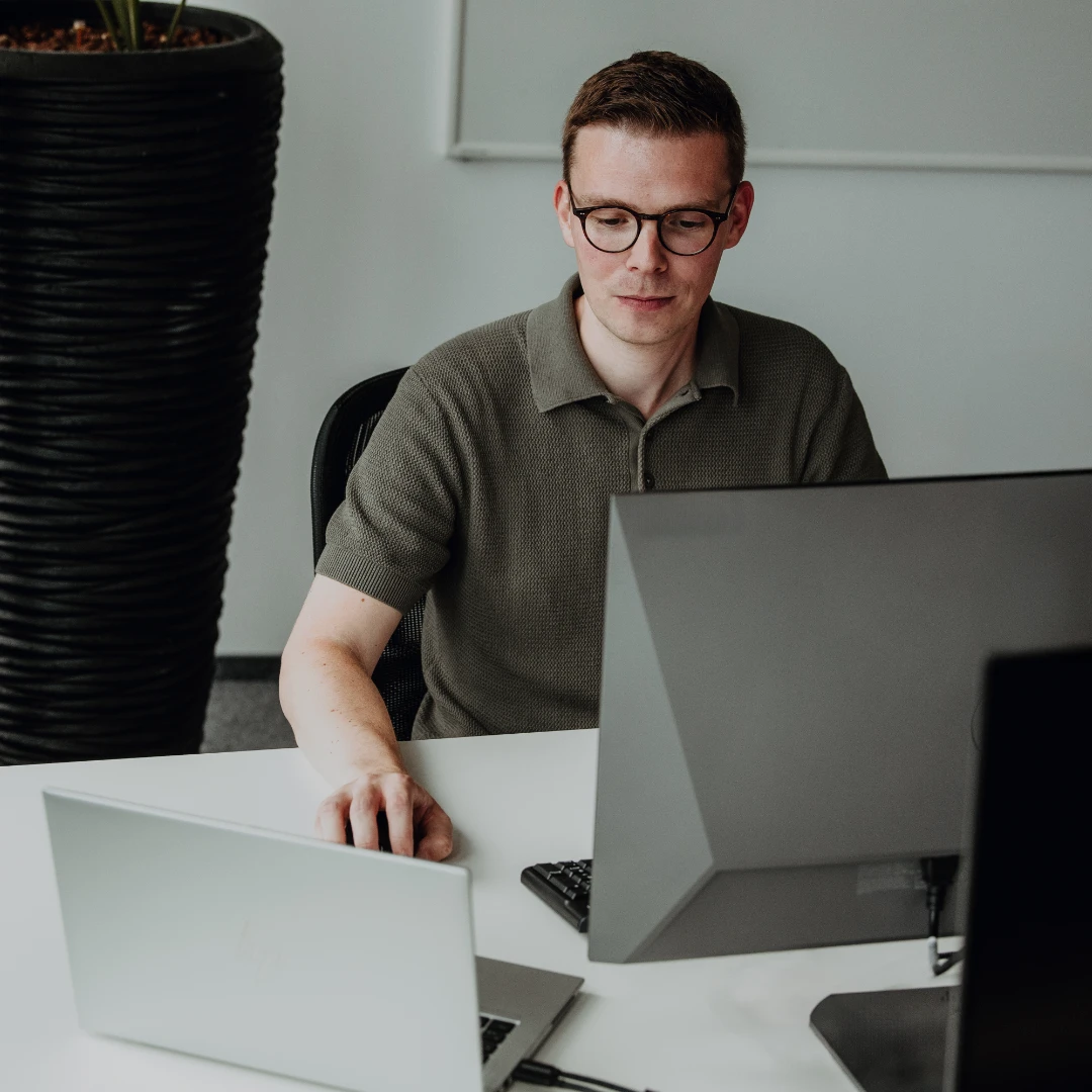Un collaboratore esperto lavora concentrato su laptop e monitor in un ufficio moderno – lavoro autonomo, competenze professionali e interessanti opportunità di sviluppo per professionisti esperti in BSI Software.