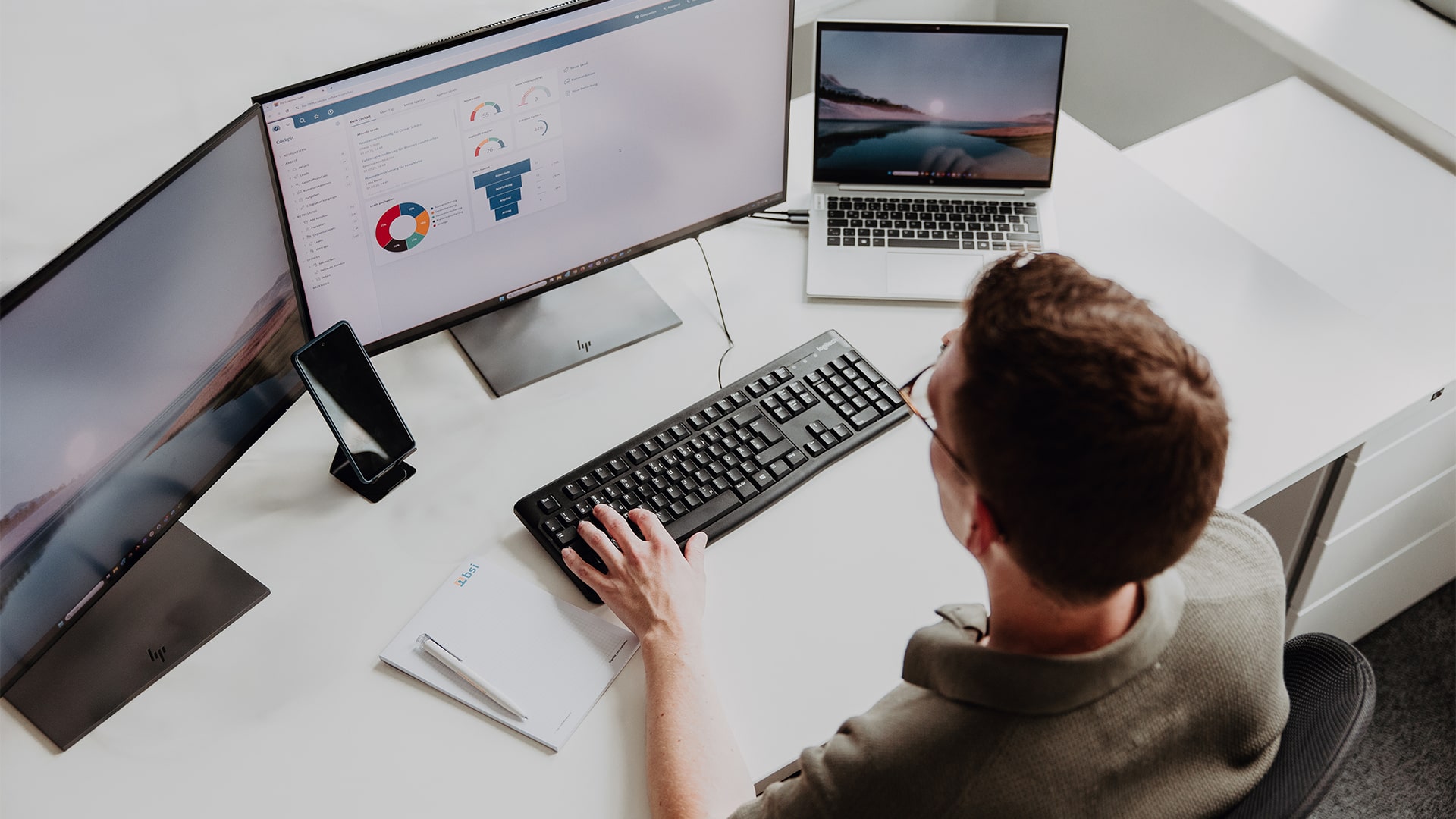 Mitarbeiter arbeitet am Schreibtisch mit drei Bildschirmen, analysiert Daten in einer CRM-Software von BSI – modernes Büro in Düsseldorf.