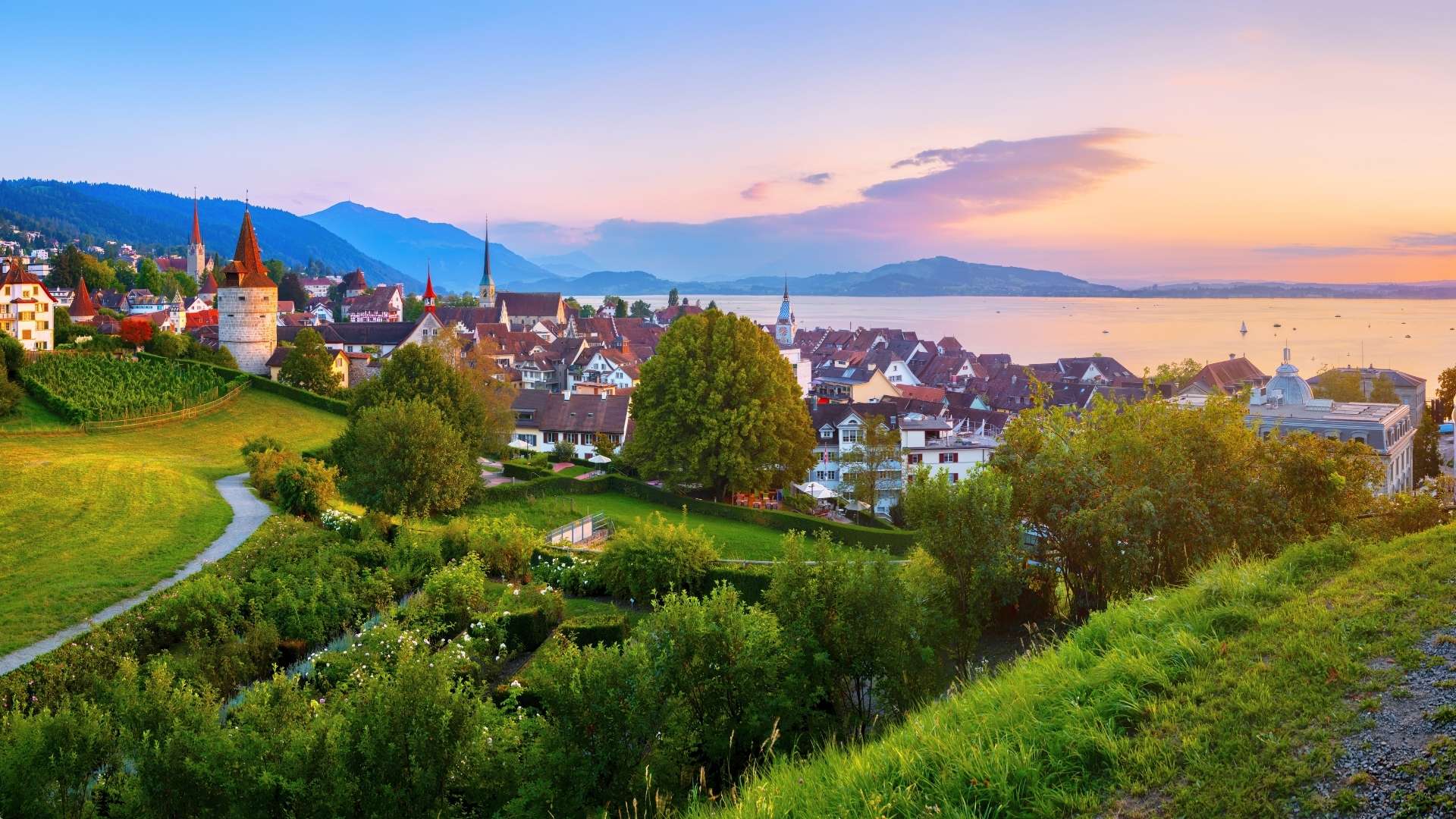 Panoramablick auf die historische Altstadt von Zug mit mittelalterlichen Türmen, farbigen Häusern und dem Zugersee vor alpiner Kulisse. Im nahegelegenen Baar befindet sich ein weiterer Standort von BSI Software in der Schweiz.