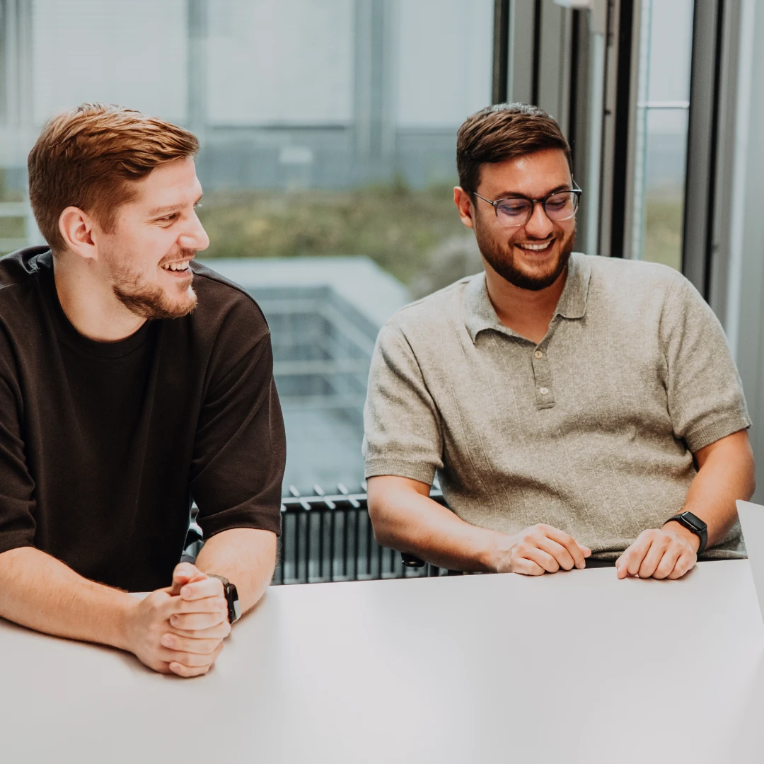 Drei Mitarbeitende sitzen gemeinsam in einem Meetingraum, lachen und diskutieren Ideen am Laptop – eine offene, wertschätzende Teamkultur und moderne Arbeitsumgebung bei BSI Software als attraktiver Arbeitsplatz.