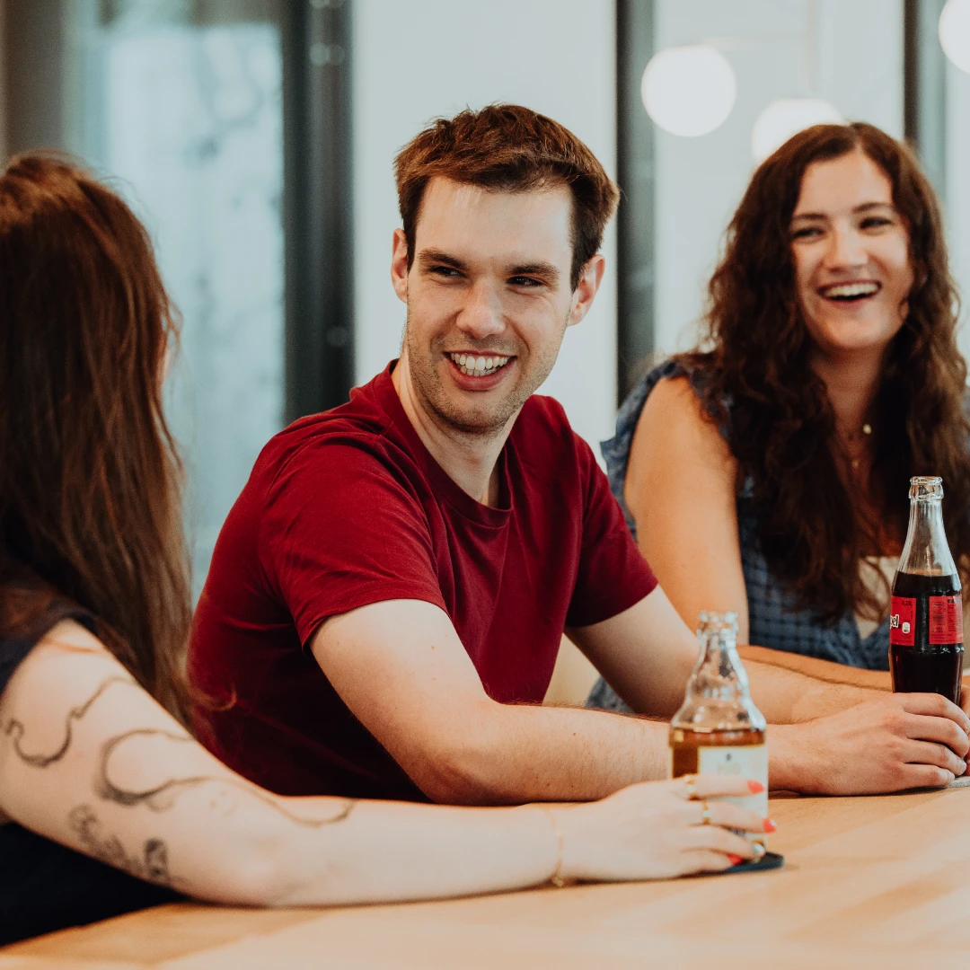 Drei Mitarbeitende sitzen entspannt zusammen, lachen und tauschen sich bei Getränken aus – eine offene, kollegiale Atmosphäre und gelebte Teamkultur bei BSI Software, die den Arbeitsalltag attraktiv und menschlich macht.
